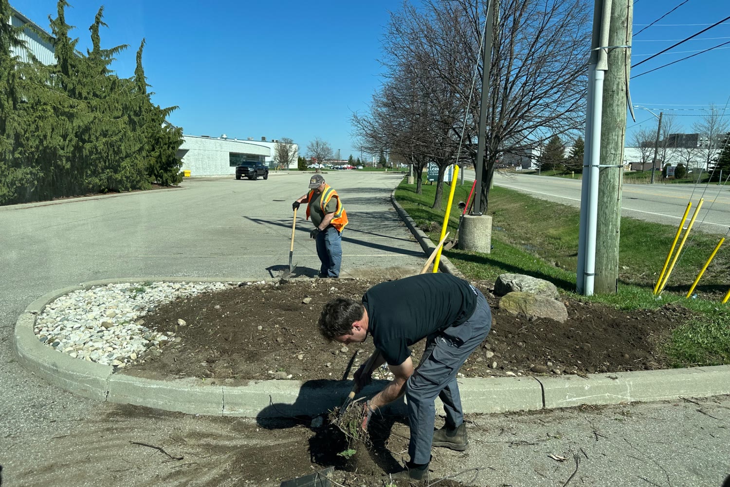 Two 4 Seasons Landscaping crew members working on a commercial property bed near a parking lot in Brantford, Ontario.