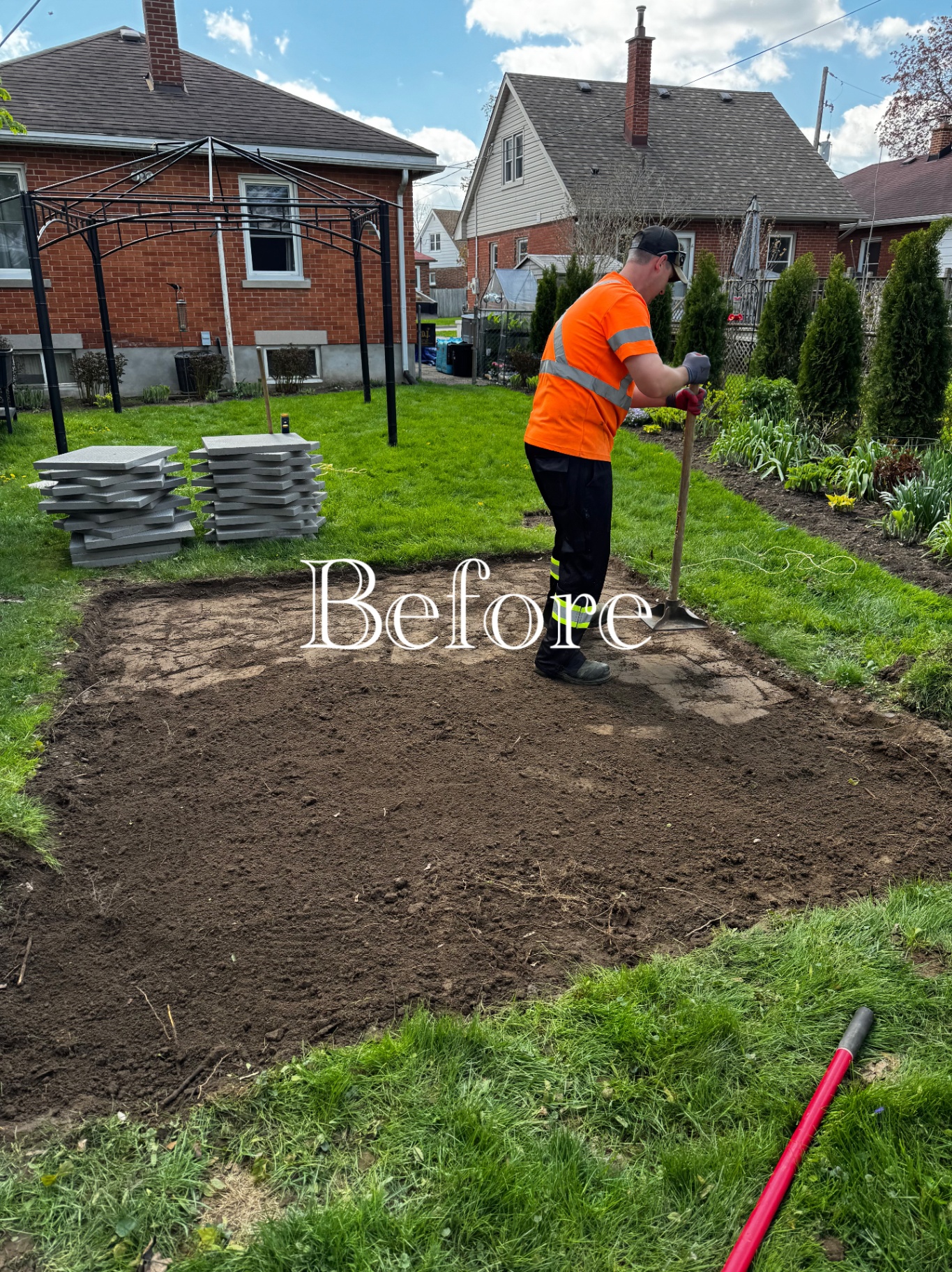 Backyard patio area excavated to soil with slabs stacked nearby and a crew member digging.
