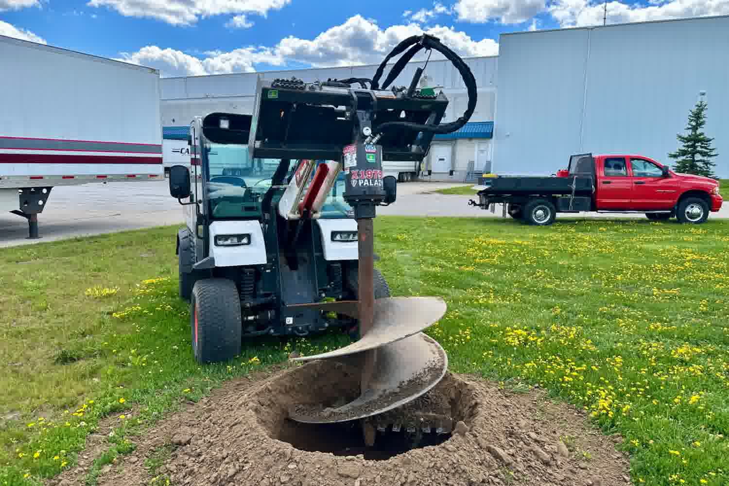 Commercial tree-planting auger mounted on a compact utility vehicle drilling a hole at an industrial property in Brantford, Ontario.
